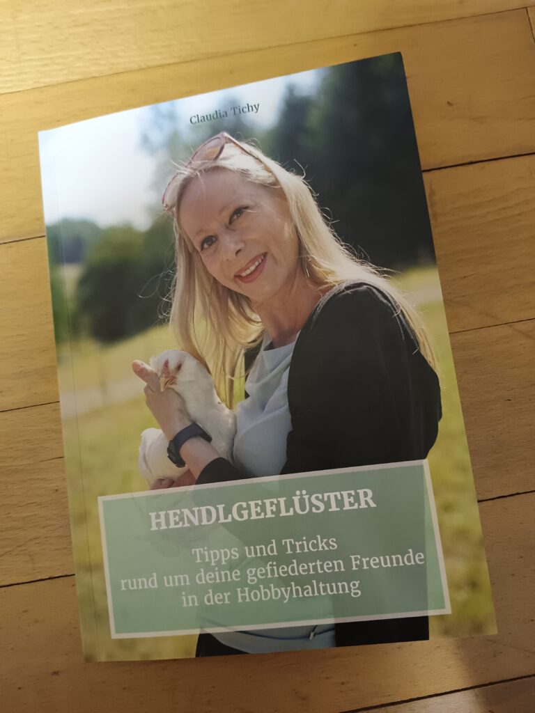 Buchcover von "Hendlgeflüster" von Claudia Tichy. Titelbild Claudia mit einem Huhn am Arm